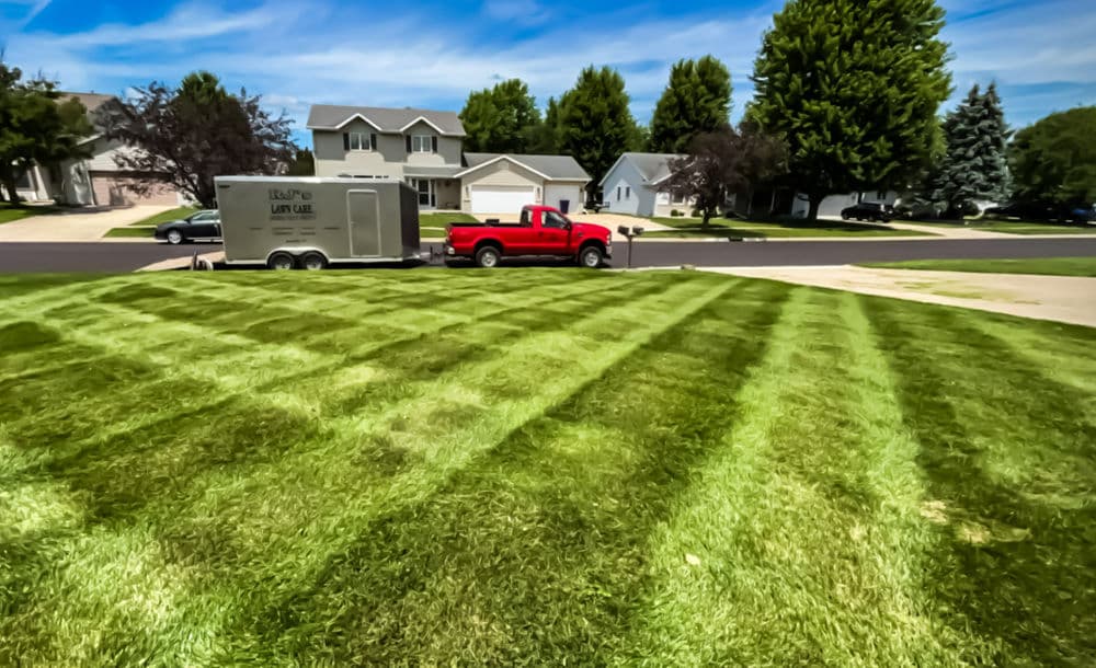 Red pickup truck parked near freshly mowed lawn with distinct striped patterns in suburban area.