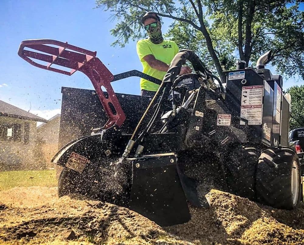 Man operating a powerful wood chipper in a yard, surrounded by flying wood shavings.