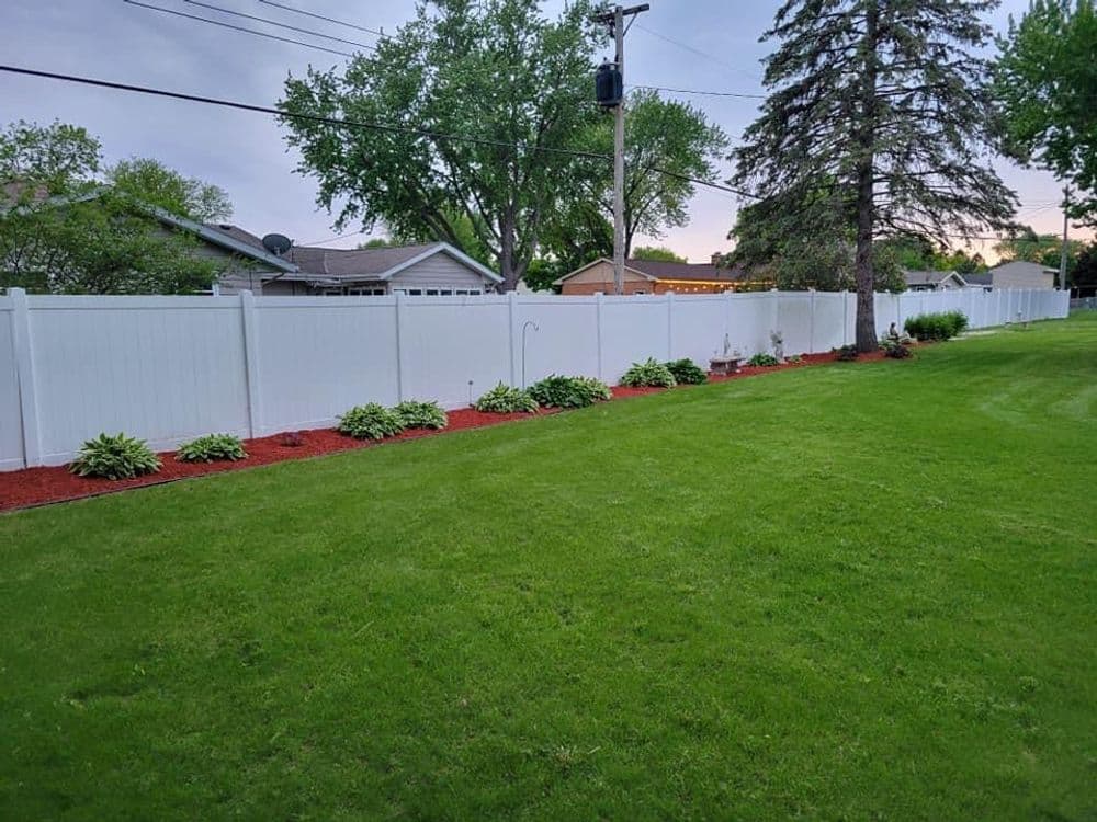 Lush green lawn with white fencing and landscaped flower beds along the border.