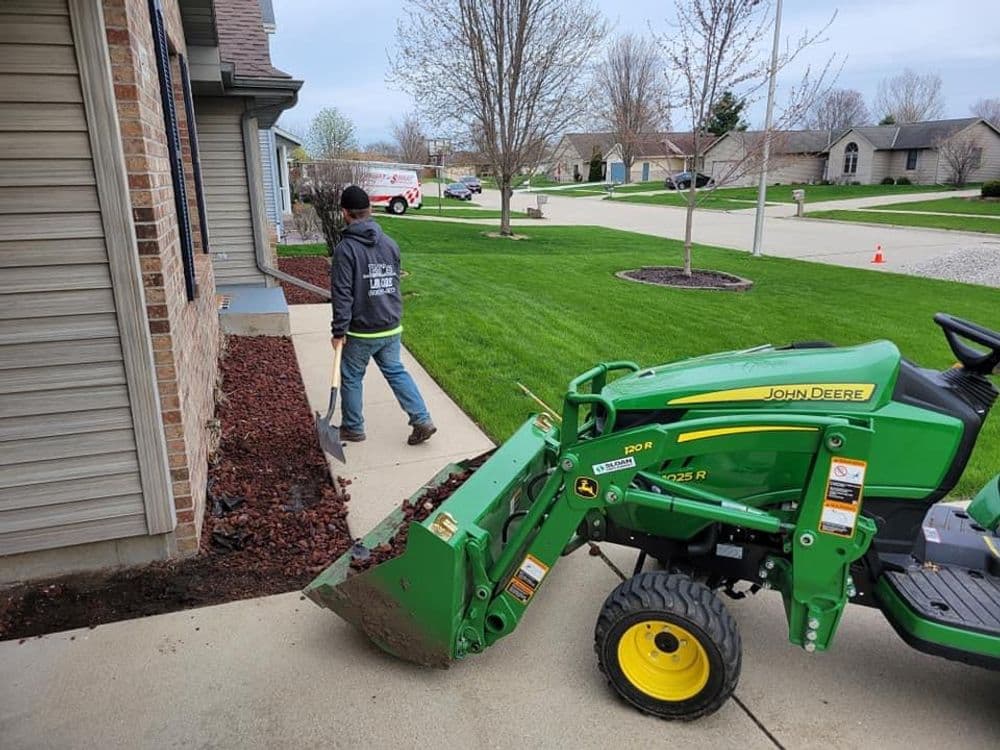 Landscaper using a John Deere tractor to maintain a residential yard and landscaping.