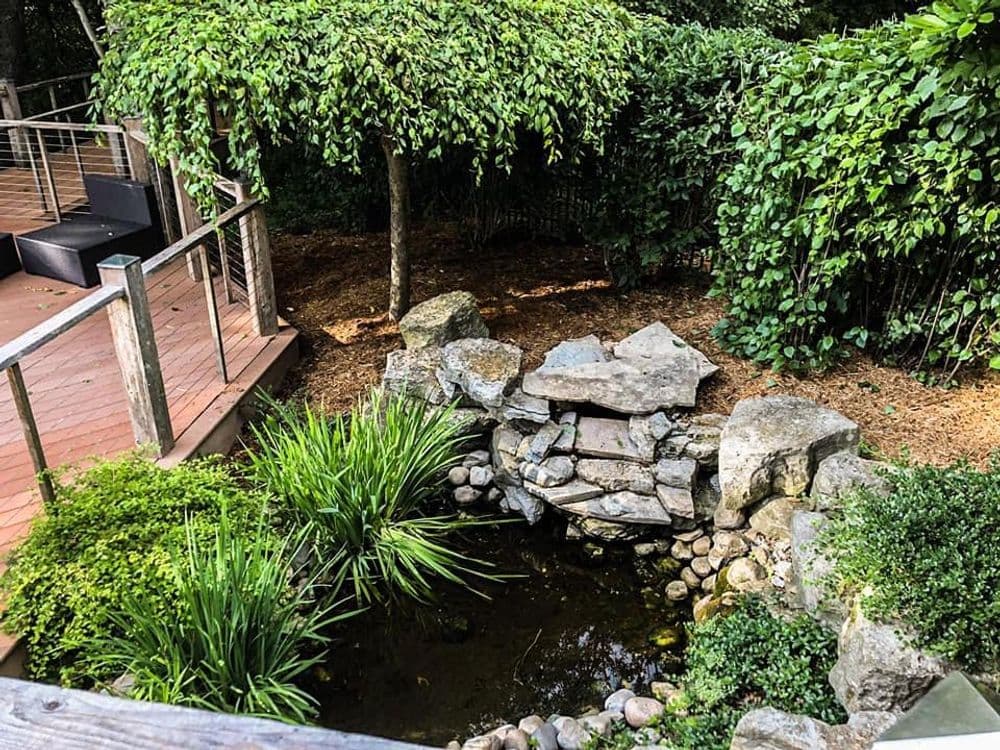 Tranquil garden with water feature, rocks, lush greenery, and wooden deck.