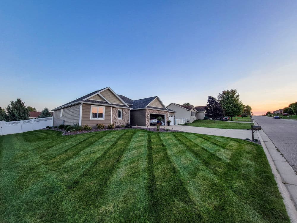 Well-maintained suburban home with striped lawn and clear blue sky at sunset.