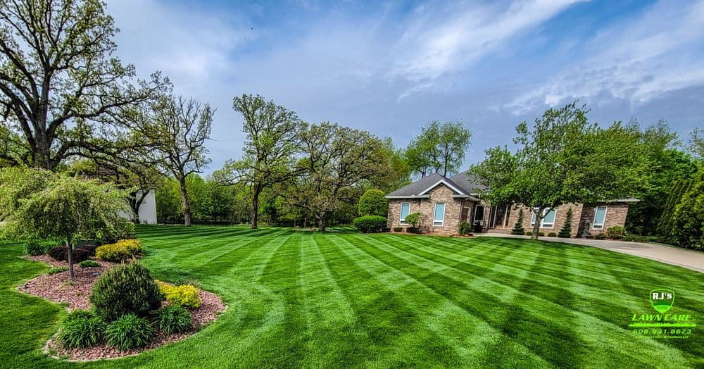 Well-maintained lawn with striped pattern, surrounded by trees and landscaped shrubs.