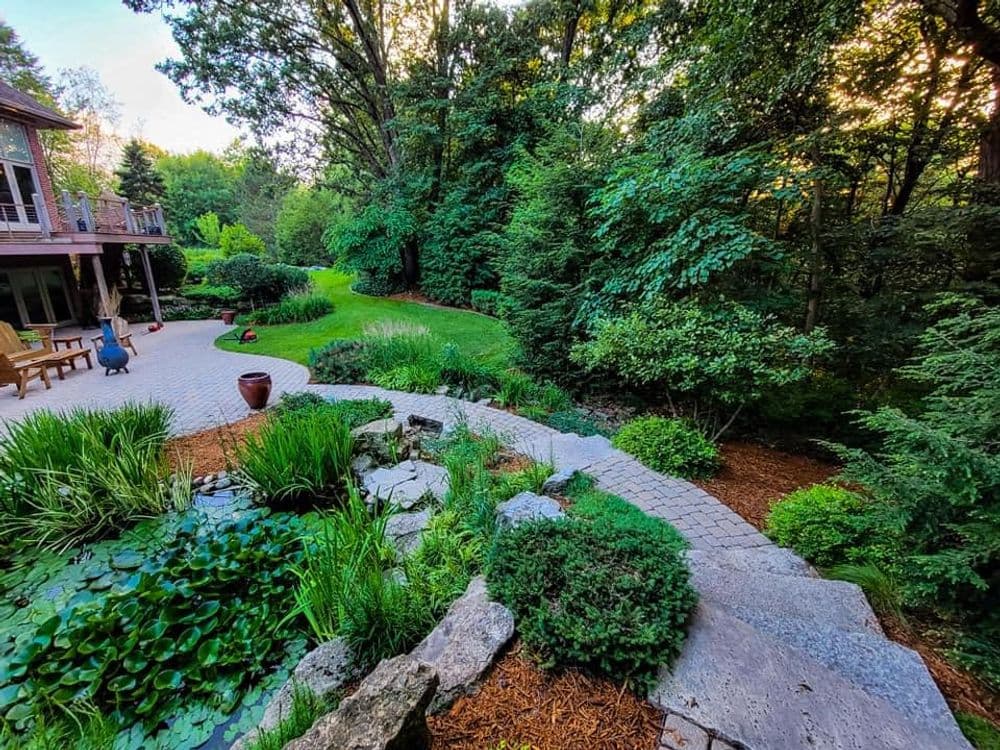 Lush garden pathway with stone steps leading through greenery and a serene landscape.