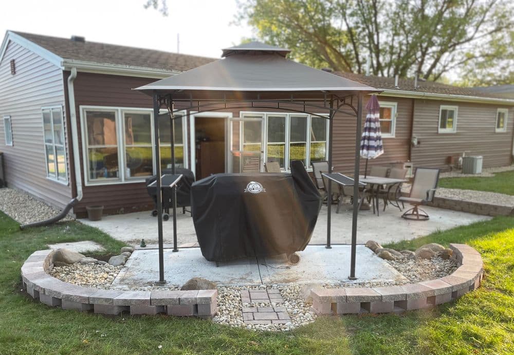 Backyard patio with gazebo and grill, surrounded by landscaping and grass. Ideal for outdoor cooking.