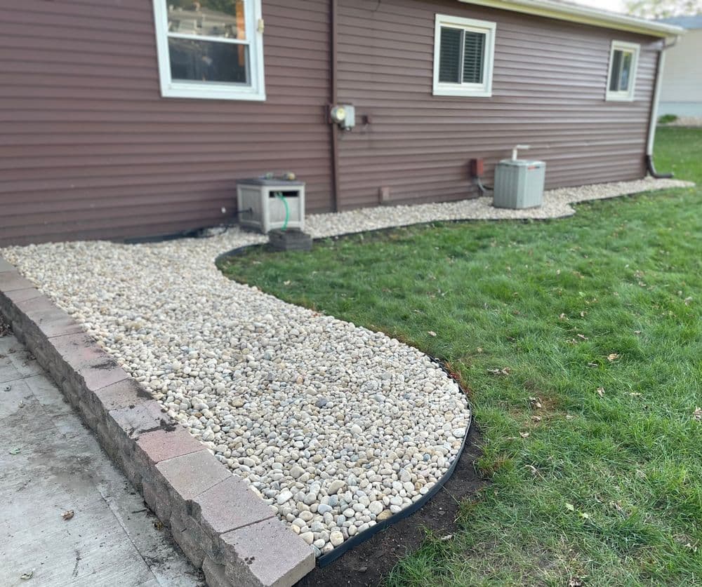 Landscaped backyard path of small gravel stones alongside a brown house exterior.