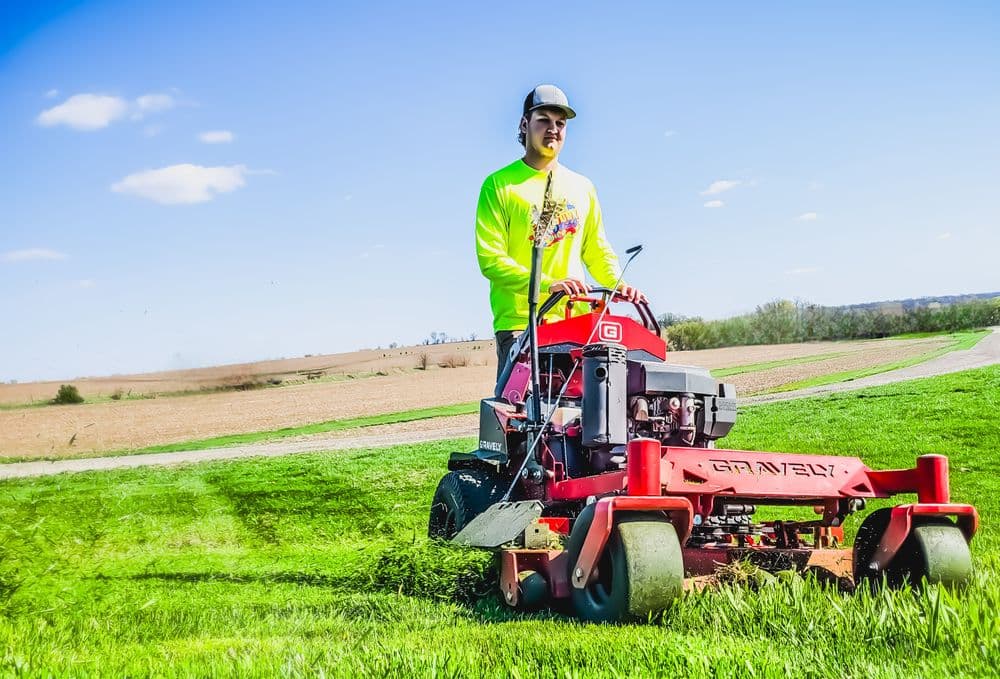 Person mowing grass with a Gravely lawn mower on a sunny day in an open field.