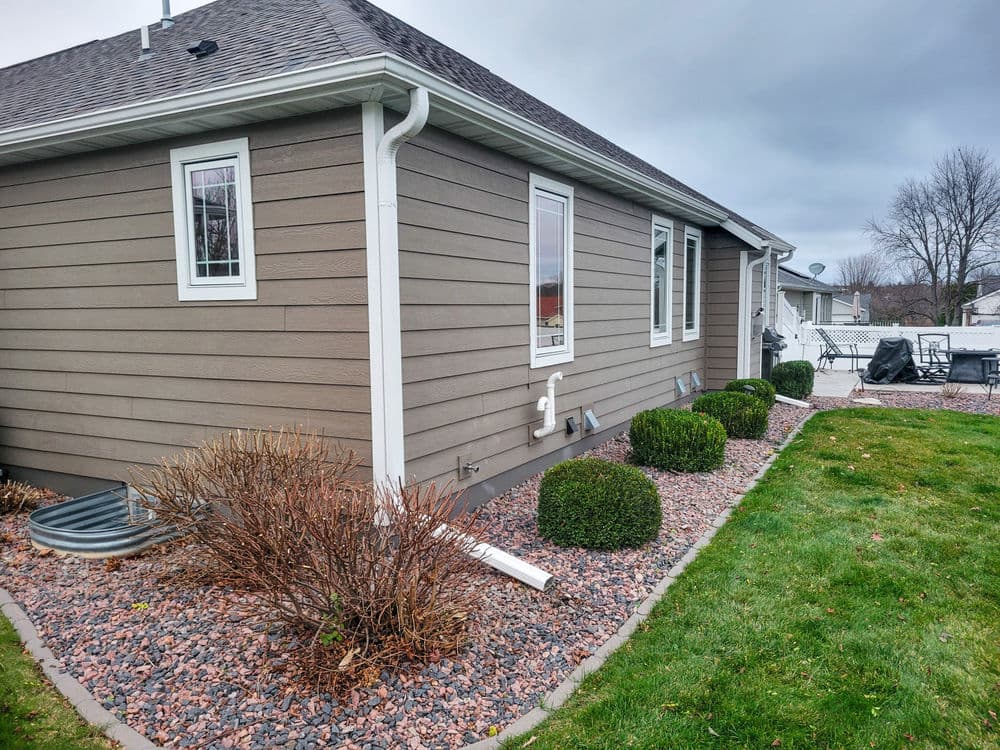 Side view of a modern house with landscaped yard featuring shrubs and gravel pathway.