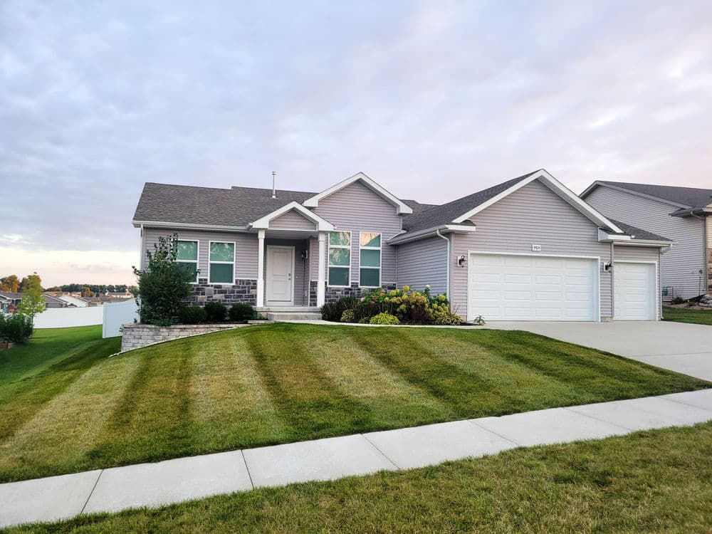 Modern single-story house with gray exterior, landscaped yard, and two-car garage.