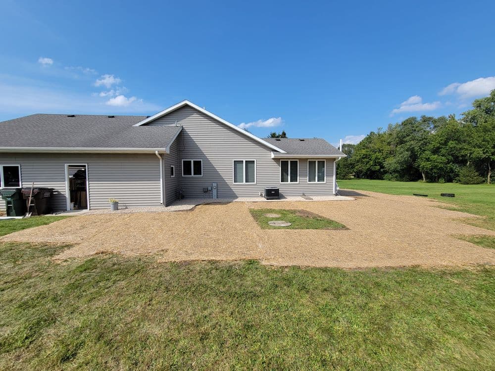 Newly landscaped backyard with straw mulch, large home exterior, and clear blue sky.