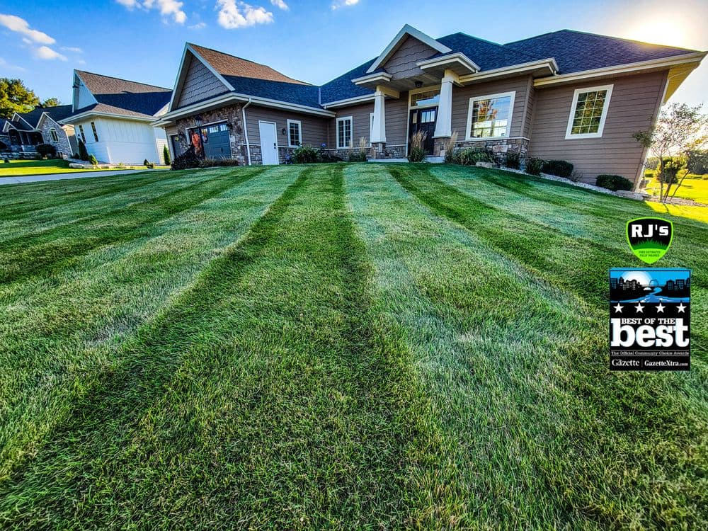 Well-manicured lawn with striped grass in front of a modern house, showcasing RJ's landscaping services.