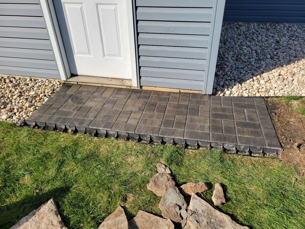 Paved walkway leading to a door, featuring dark pavers and surrounding gravel landscaping.