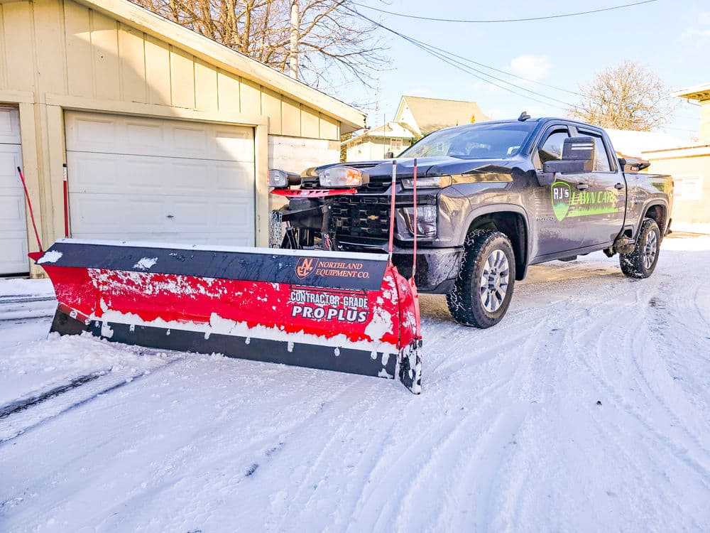 Snow removal truck with a plow parked in a snowy driveway. Ideal for winter service promotions.