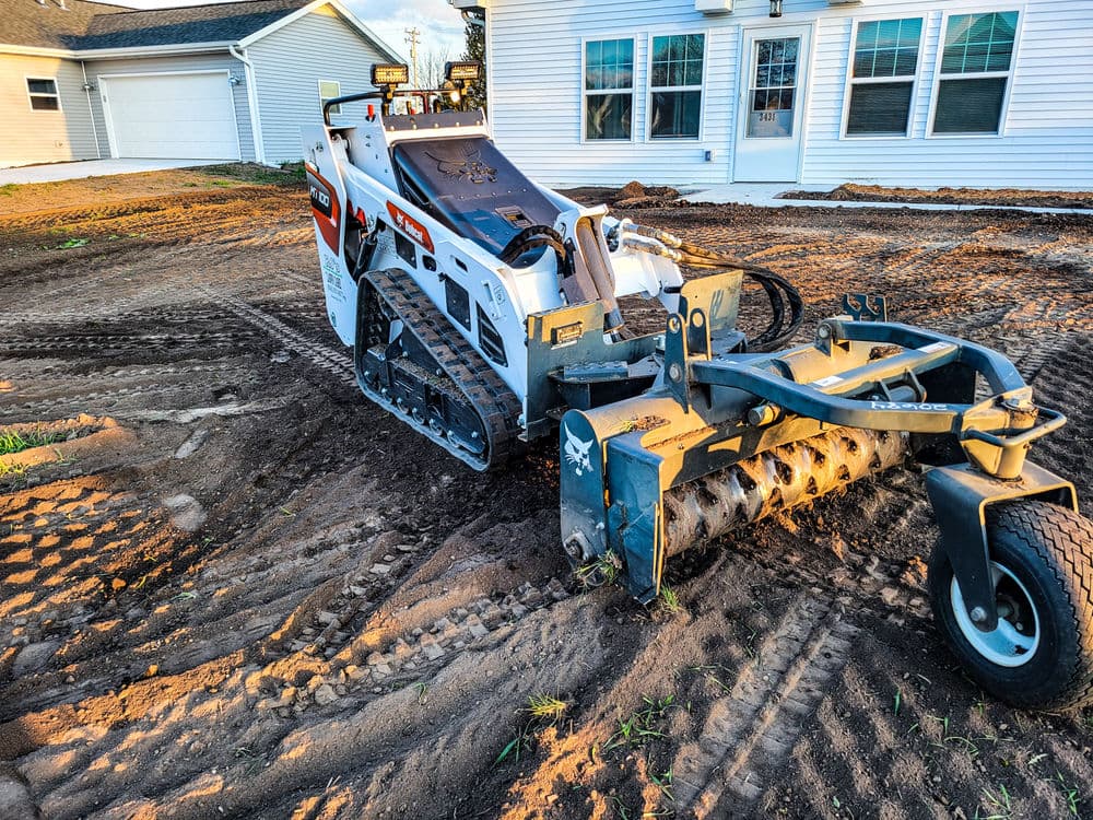 Bobcat skid steer with a rotary tiller on a construction site preparing soil for landscaping.