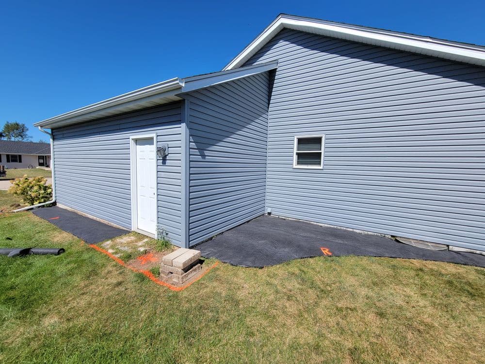 Newly installed landscape fabric and edging around a gray house exterior.
